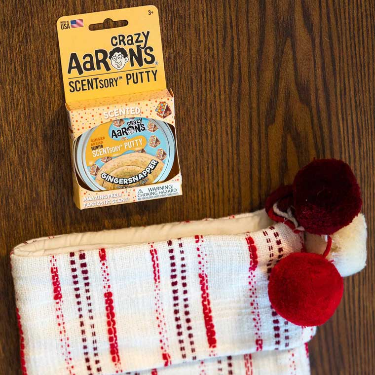 Package of Gingersnapper SCENTsory™ Thinking Putty® next to a stocking on a wood table.